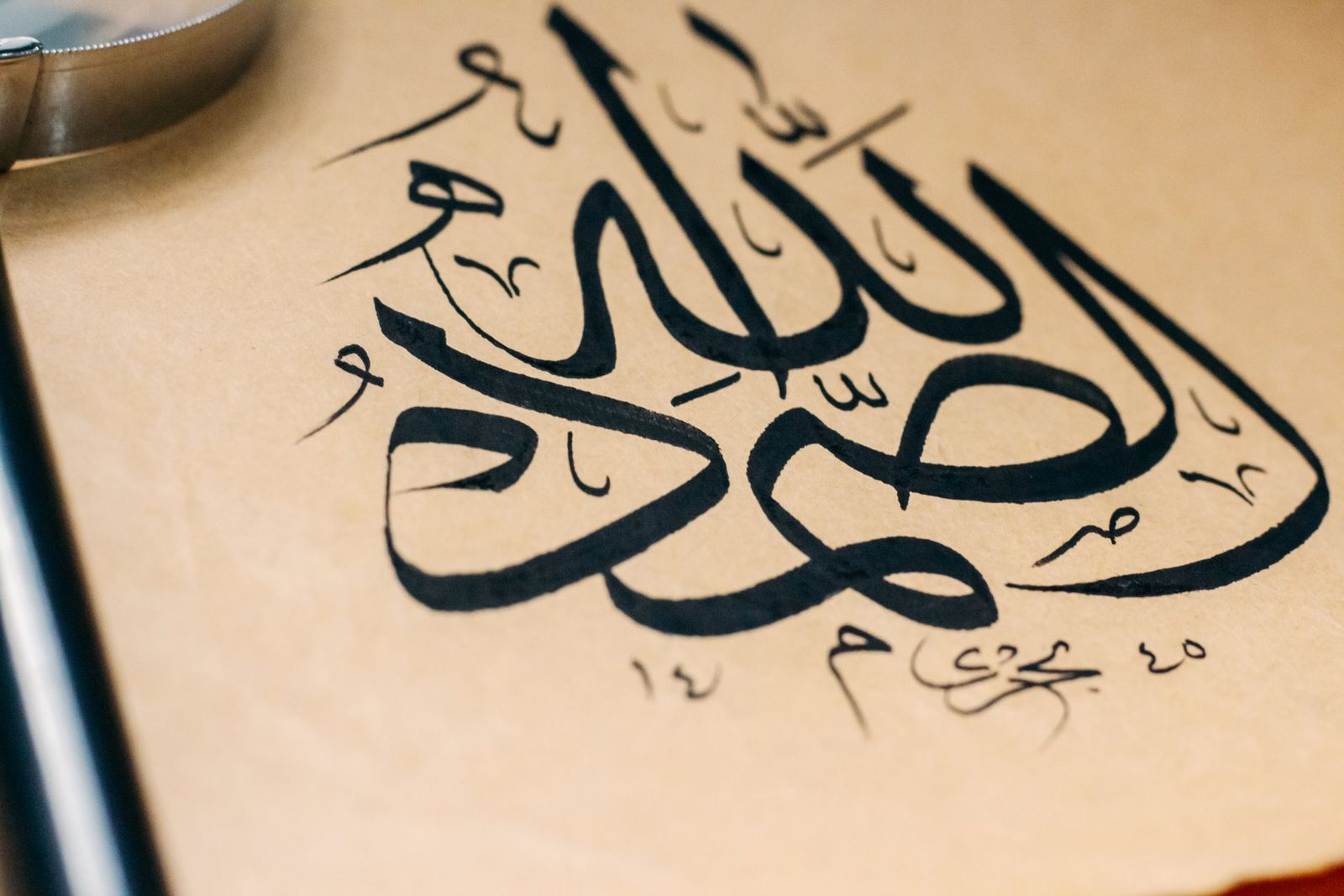 Main d’un calligraphe traçant des lettres arabes à l’encre sur du papier vergé