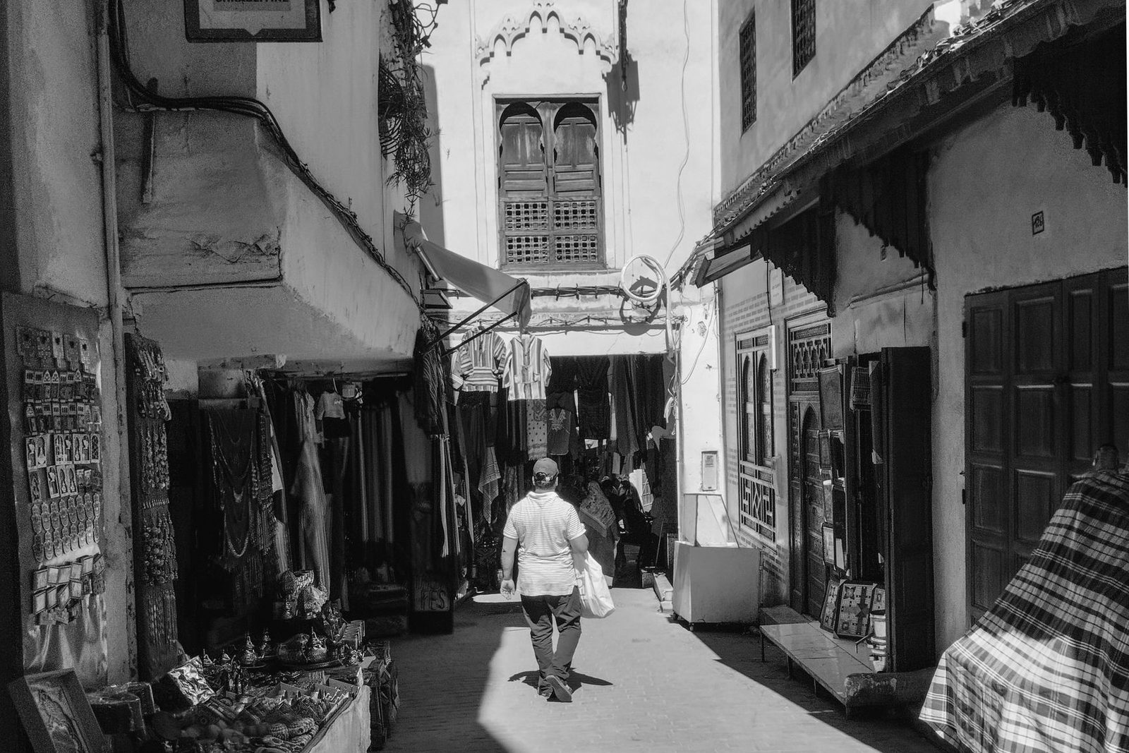 Ruelle étroite de la médina de Fès baignée de lumière, murs ocres et étals d’artisans