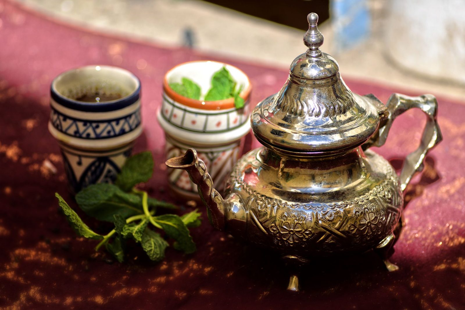 Thé à la menthe versé de haut dans un verre décoré, mousse légère, théière en métal ciselé
